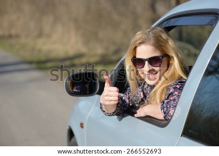 Woman driver happy smiling showing thumbs up coming out of car window