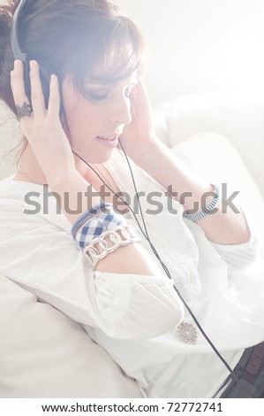 Happy woman with headphones lying down on sofa in lounge, listen to music