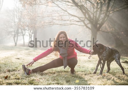 Woman and her dog stretching outdoor. Fitness girl and her pet working out together.