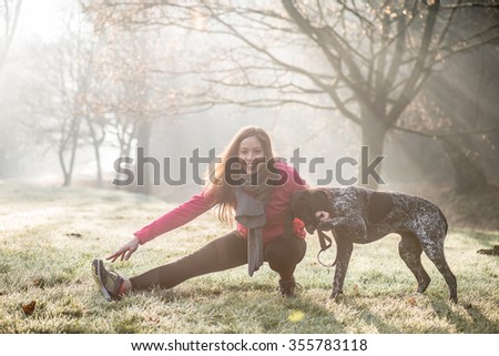 Woman and her dog stretching outdoor. Fitness girl and her pet working out together.