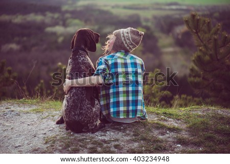 Woman and her dog posing outdoor. Girl loving and hugging tightly her dog and watching landscape.