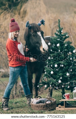 Girl with horse decorating Christmas tree. Funny outdoor image.