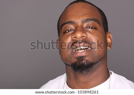 Portrait of a young black man with gold teeth and necklace.