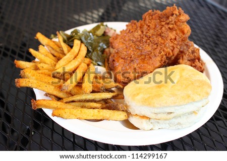 Southern style meal with fried chicken, collard greens with bacon, French fries, and a biscuit.