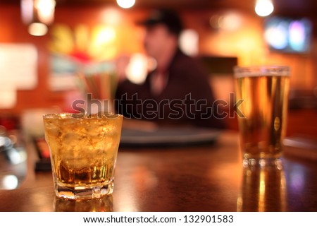 Whiskey on the rocks and a glass of beer in the background at a dive bar.