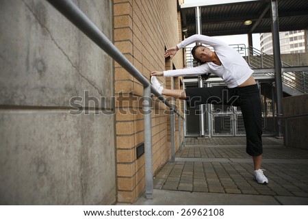 A young woman in fitness clothes stretching on a hand rail.