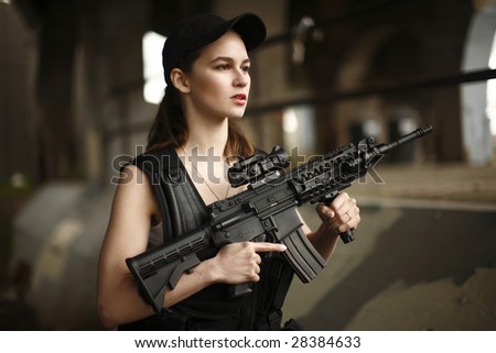 A young and attractive woman holding an assault rifle safely with her finger off the trigger.