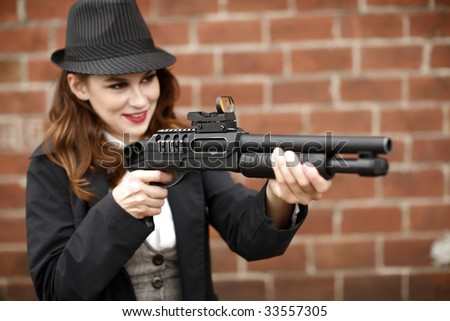 A young and stylish woman pointing a shotgun with a smile.