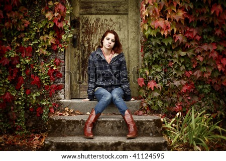 Portrait of a young and pretty woman sitting on steps next to colorful leaves.