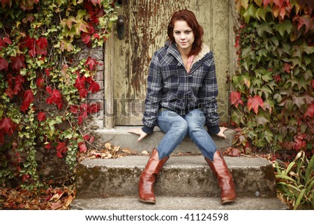 Portrait of a young and pretty woman sitting on steps next to colorful leaves.