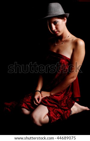 Woman wearing red satin sheet and fedora.