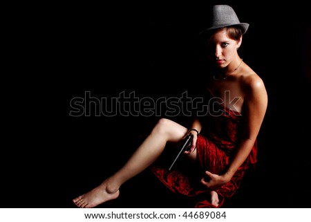 Woman wearing red satin sheet and fedora and holding a pistol