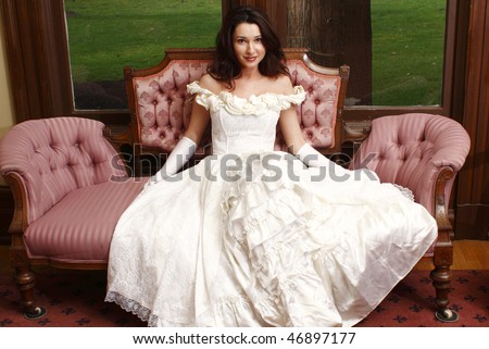 Woman wearing vintage dress sitting on antique sofa.