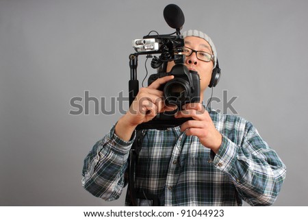 Man shooting video with a digital SLR camera with shotgun microphone and separate audio recorder.