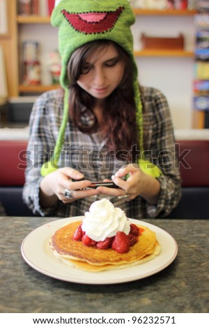 Young woman texting on cellphone at breakfast in a cafe. (Soft Focus. Shallow DOF)