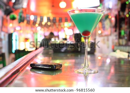 A Blue Hawaiian cocktail and cellphone at a bar.