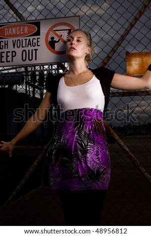 Wild woman standing against a fence with a high voltage sign