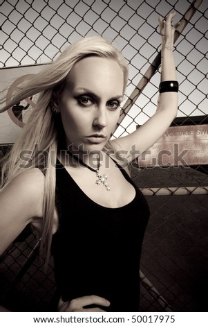 young female model holding on to a wire fence, next to a danger dign