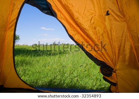 Kind from tent on lawn with green grass and blue sky