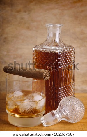 still life composition with glass and bottle of whiskey and cigar on a wooden vintage background