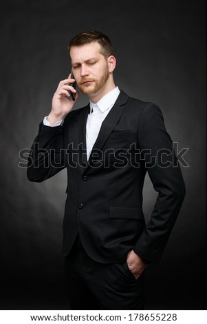 young handsome skeptical businessman talking serious on smart phone device on a dark background