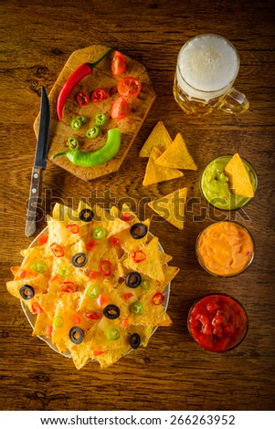 nachos on a plate with salsa, cheese and guacamole dip and beer mug