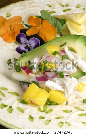 A spring plate of avocado stuffed with crabmeat, mango, red onions, and chives in a lemony vinaigrette surrounded by pansy flowers