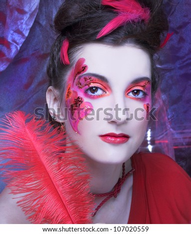 Woman in red. Young lady with artistic make-up and with feathers in her hair.