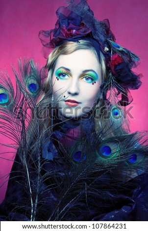 Portrait of young woman in creative image and in hat with peacock feathers