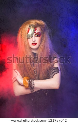 Young woman in artistic image with one-eyed visage posing with smoke