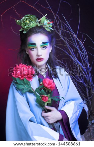 Young woman in creative image in eastern style with flowers in hair and in kimono.