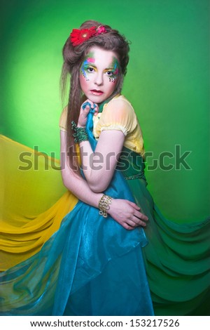 Spring fairy. Young woman in creative image posing with bright fabric\'s and flowers.