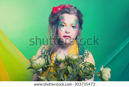 Spring fairy. Young woman in creative image posing with bright fabric\'s and flowers.