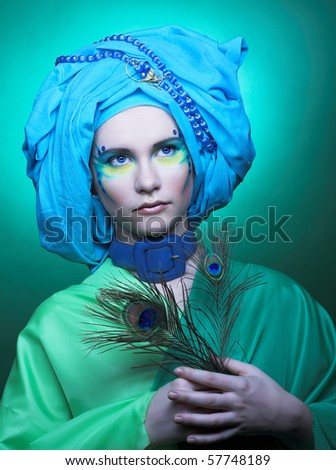 Young woman with creative make-up in blue turban with peacock feathers