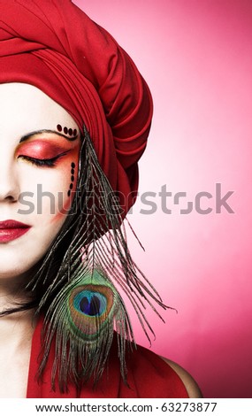 Portrait of young woman in vintage style in red turban with peacock plume