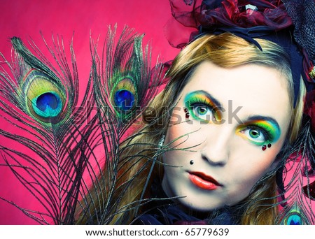 Portrait of young woman in creative image and in hat with peacock feathers