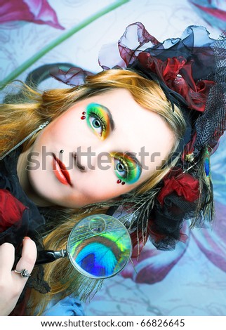 Creative lady in hat with feathers and with loupe.