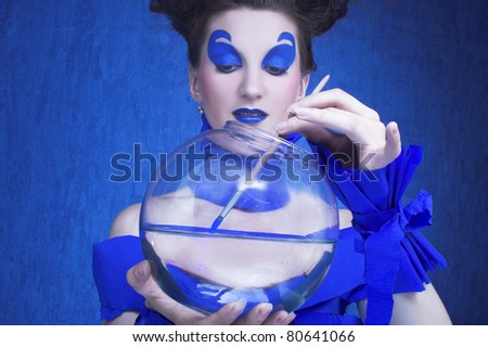 Creative young woman in  blue with sphere aquarium and brush in her hands