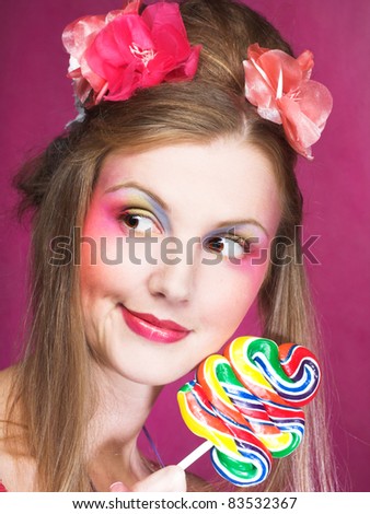 Portrait of young woman with lollipop and with pink flowers in her hair