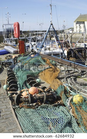 fishing nets and deep sea fishing equipment lying on pier with harbour scene