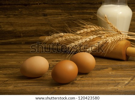 Three eggs , jug with milk and wheat seeds on the wooden table.