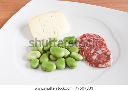 broad beans with pecorino cheese and salami slices on a white plate