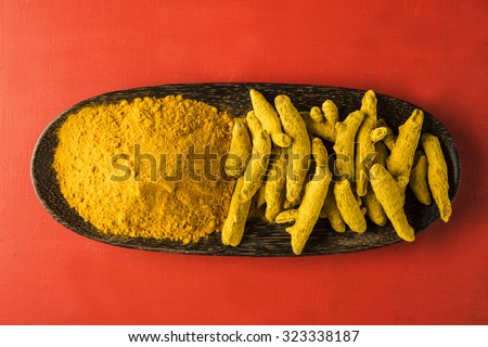 dry Turmeric and turmeric powder in wooden plate over red background , horizontal and top view