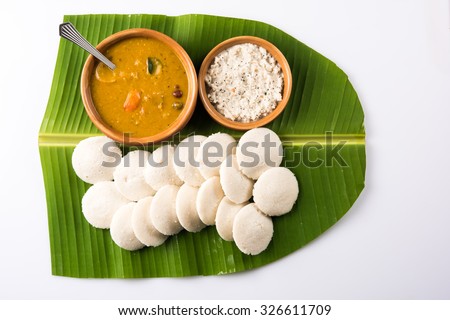traditional south indian food or recipe idli or idly with sambar or sambhar and coconut chutney in earthen bowl over green banana leaf on white background, top view isolated