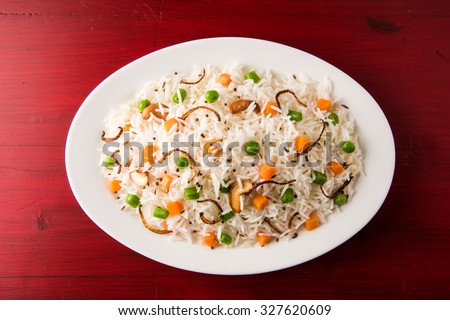 Indian Pulav or vegetables rice or veg biryani / vegetable biryani, Basmati Rice served in a white oval shaped ceramic plate, isolated on red wooden background, closeup and top view