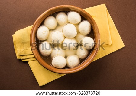 Rasgulla or rosogulla - an Indian sweet made from khoya, soft and spongy, in earthen bowl over yellow napkin and brown background, top view closeup, isolated