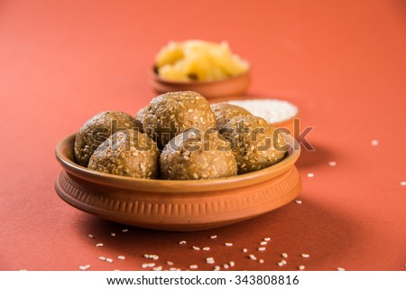 The indian sesame sweet or tilgul laddu, made up of jaggery and sesame seeds, indian sweet for Makar Sankranti festival, in terracotta bowl with jaggery & raw sesame, isolated on brown background