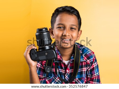 10 year old indian boy holding digital camera or DSLR camera, posing like a professional photographer, young photographer, kid photographer, child photographer, portrait, closeup, yellow background