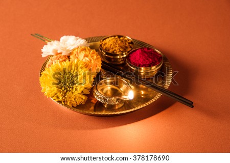 Beautifully Decorated Pooja Thali for diwali celebration to worship, huldi or turmeric powder and kumkum, flowers, scented sticks in brass plate on orange background, hindu puja thali