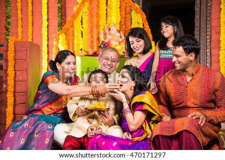 group photo of cheerful indian family in ganesh festival while eating sweets, happy indian family eating sweet meets in ganpati festival or ganesh utsav